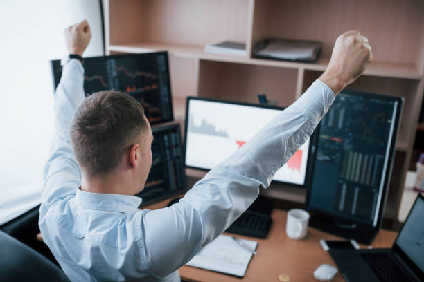 istock Hands up because of success. Man working online in the office with multiple computer screens in index charts 1145204430