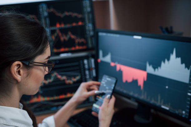 istock In eyeglasses. Woman working online in the office with multiple computer screens in index charts 1145204692