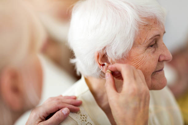 Female doctor applying hearing aid to senior woman's ear Female doctor applying hearing aid to senior woman's ear hearing loss photos stock pictures, royalty-free photos & images