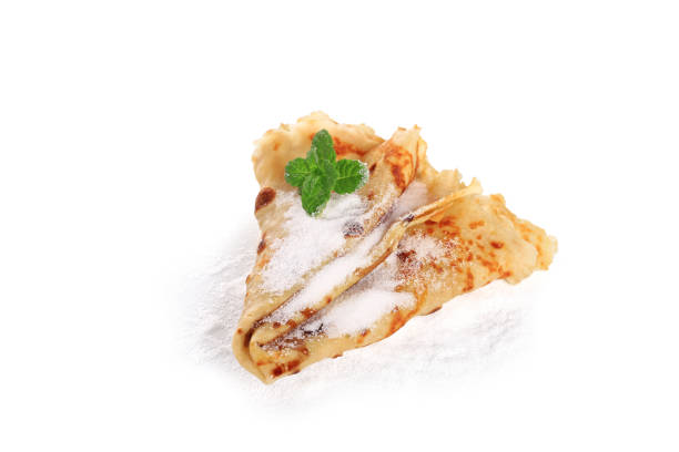 Homemade  European thin  pancakes rolled up on a white plate Delicious French pancakes rolled up  decorated with purple violets on a  white plate with white background