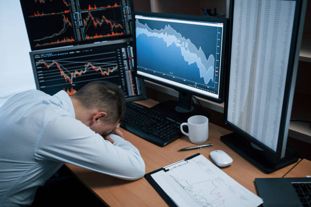 istock Tired of hard day. Man working online in the office with multiple computer screens in index charts 1145214253