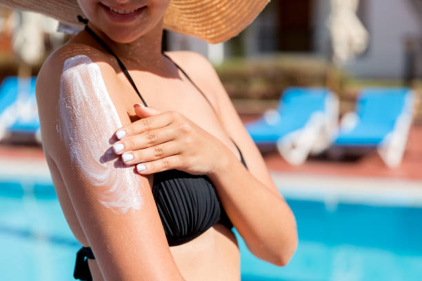pretty woman applying sun cream with her hands on tanned shoulder by the pool on sunny summer day. sun protection factor in vacation, concept - spray tan body human skin imagens e fotografias de stock