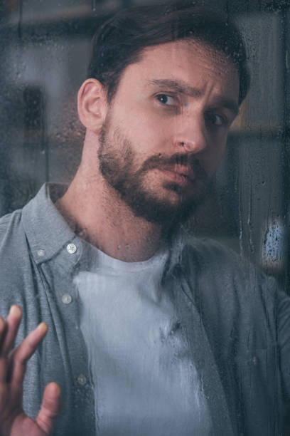 istock handsome upset man touching window with raindrops and looking away 1145223729