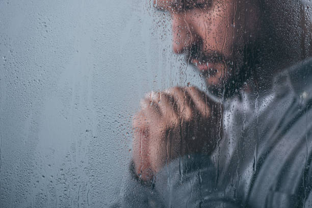 istock upset man with folded hands through window with raindrops and copy space 1145223737
