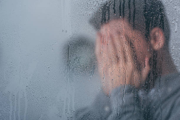 istock selective focus of raindrops on window with man covering face and crying on background 1145223742