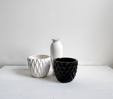Vase, black-and-white pots on wood table. White wall, background with sunlight and shadows. Modern interior. Minimalism style.