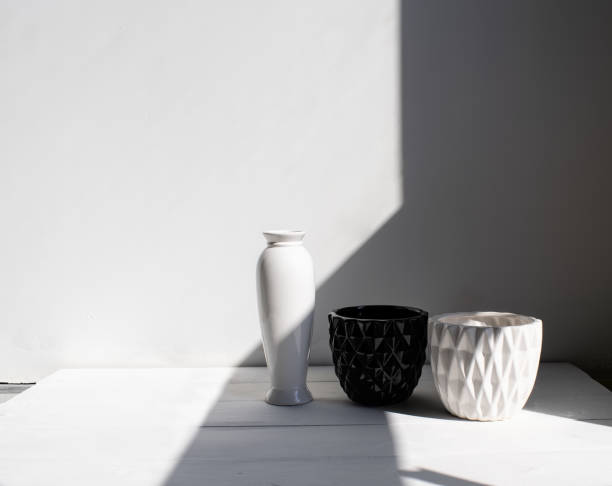 istock Vase, black-and-white pots on wood table. White wall, background with sunlight and shadows. Modern interior. 1145223958