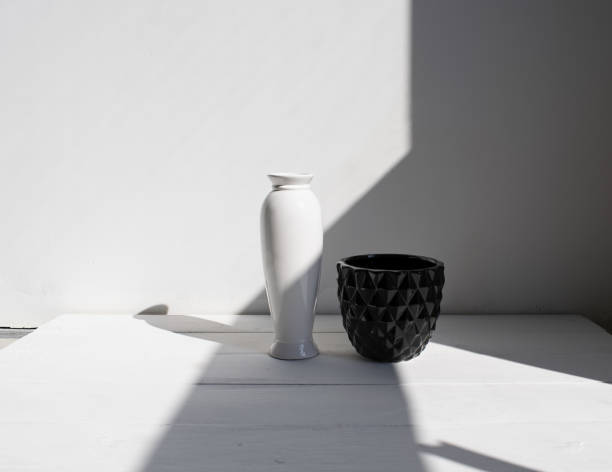 istock Black pot with white vase on wood table. White wall, background with sunlight and shadows. 1145223985