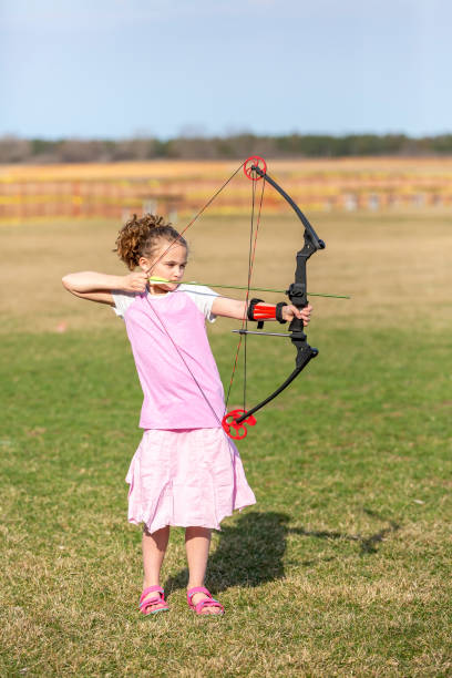 istock Young Girl Practicing Archery with Bow & Arrow Outdoors 1145226242