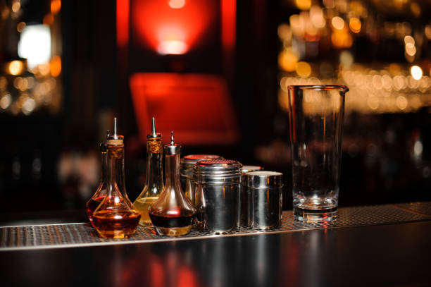 Bartender equipment such as bottles, measuring glass cup and spice shakers on the bar counter in the blurred background