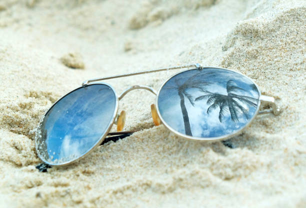 istock Mirrored sunglasses close up on the beach sand with palm trees reflection 1145229542