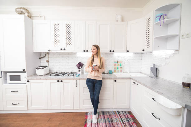 istock Adorable nice girl drinking coffee, sitting on table countertop in modern light white kitchen 1145232080