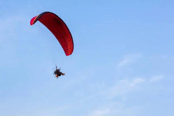 Photo of Adventure man active extreme sport pilot flying in sky with paramotor engine glider parachute. Paramotor flying on the sky at sunset.