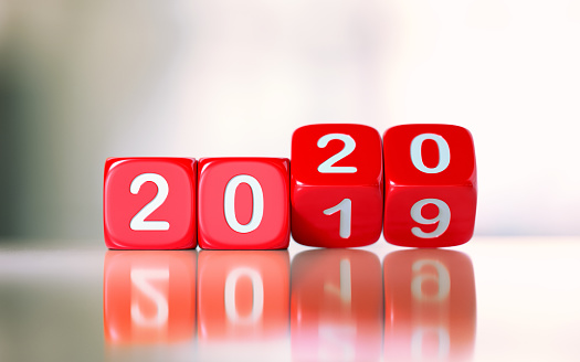 Red dices are changing from 2019 to 2020. Numbers are engraved on dices. Dices are lit from the upper left corner of the composition and casting shadows over defocused background. New year and change concept.  Horizontal composition with copy space.