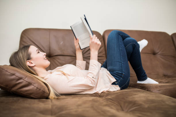 istock Happy young woman reading book on couch at home 1145236331