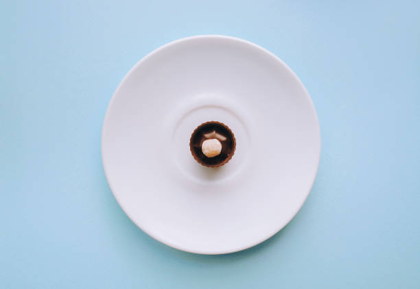 ヘーゼルナッツを持つ1つのチョコレートキャンディーは白いプレートにあります。青の背景。 - nut pastry brownie hazelnut ストックフォトと画像