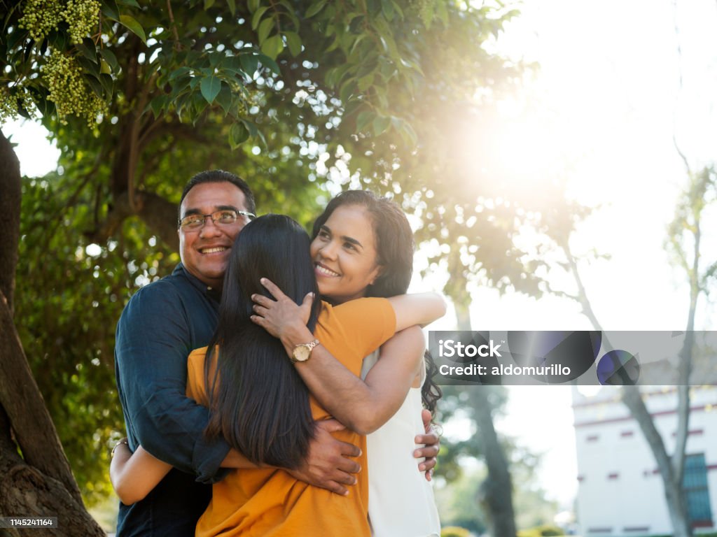 Latin young woman hugging her parents A back shot of a latin woman embracing both of her parents as they look away from camera and smile. Family Stock Photo