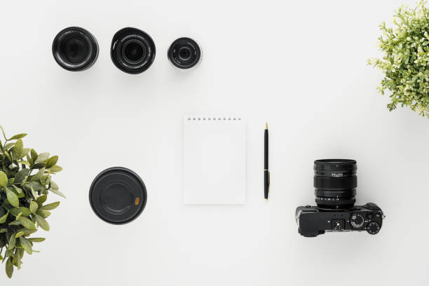 istock Mocap work photographer on a white table. Flat lay mirrorless camera, a few lenses and a notebook with a pen. 1145249081