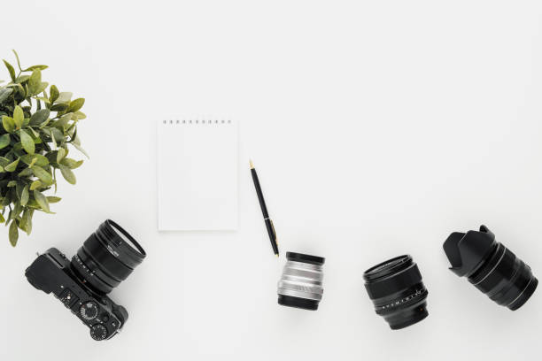 istock Mocap work photographer on a white table. Flat lay mirrorless camera, a few lenses and a notebook with a pen. 1145249086