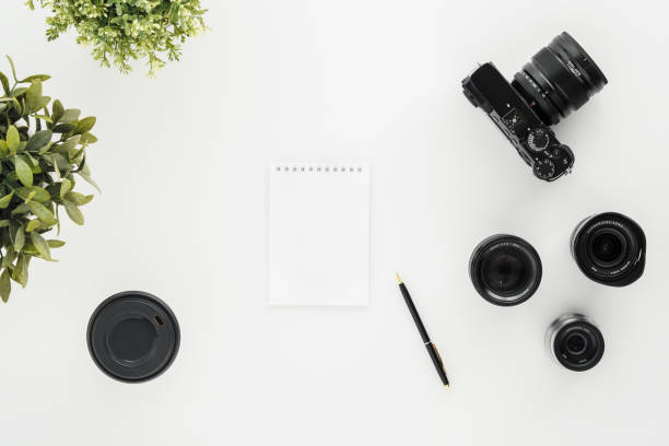 Mocap work photographer on a white table. Flat lay mirrorless camera, a few lenses and a notebook with a pen.