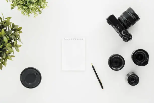 Photo of Mocap work photographer on a white table. Flat lay mirrorless camera, a few lenses and a notebook with a pen.