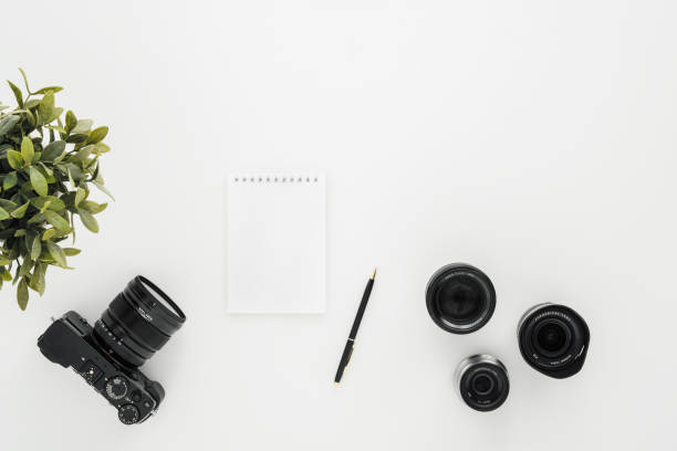 istock Mocap work photographer on a white table. Flat lay mirrorless camera, a few lenses and a notebook with a pen. 1145249127