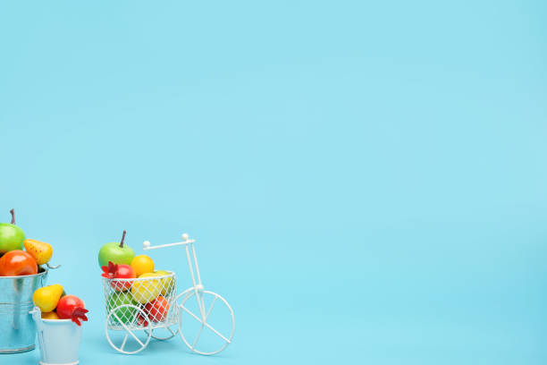 bicicleta de alambre blanco con una cesta llena de mini fruta. cerca del cubo con verduras y frutas. fondo azul. concepto de recolección y entrega de frutas y hortalizas. - abundance apple red yellow fotografías e imágenes de stock