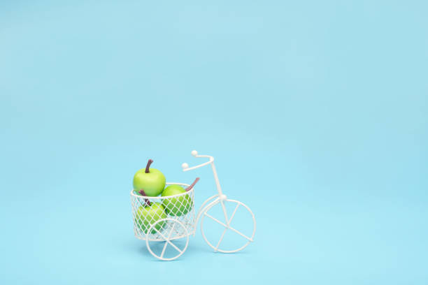 bicicleta de alambre blanco con una cesta llena de mini fruta. cerca del cubo con verduras y frutas. fondo azul. concepto de recolección y entrega de frutas y hortalizas. - abundance apple red yellow fotografías e imágenes de stock