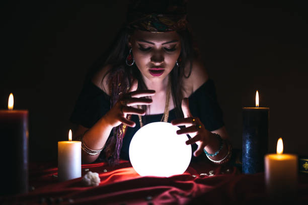 Fortune teller and crystal sphere Young female fortune teller is looking into glowing crystal sphere fortune teller photos stock pictures, royalty-free photos & images