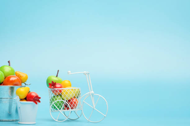 bicicleta de alambre blanco con una cesta llena de mini fruta. cerca del cubo con verduras y frutas. fondo azul. concepto de recolección y entrega de frutas y hortalizas. - abundance apple red yellow fotografías e imágenes de stock