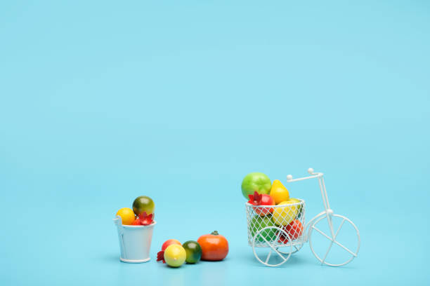 bicicleta de alambre blanco con una cesta llena de mini fruta. cerca del cubo con verduras y frutas. fondo azul. concepto de recolección y entrega de frutas y hortalizas. - abundance apple red yellow fotografías e imágenes de stock