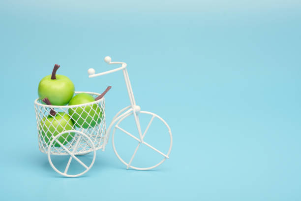 bicicleta de alambre blanco con una cesta llena de mini fruta. cerca del cubo con verduras y frutas. fondo azul. concepto de recolección y entrega de frutas y hortalizas. - abundance apple red yellow fotografías e imágenes de stock