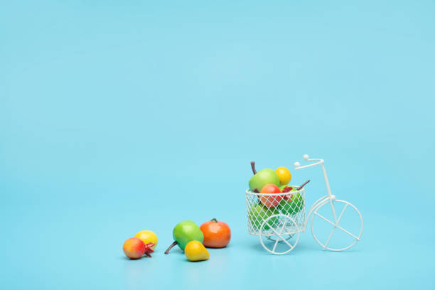 bicicleta de alambre blanco con una cesta llena de mini fruta. cerca del cubo con verduras y frutas. fondo azul. concepto de recolección y entrega de frutas y hortalizas. - abundance apple red yellow fotografías e imágenes de stock