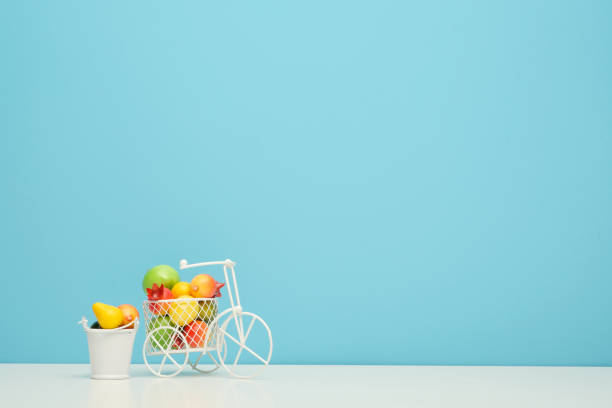 bicicleta de alambre blanco con una cesta llena de mini fruta. cerca del cubo con verduras y frutas. fondo azul. concepto de recolección y entrega de frutas y hortalizas. - abundance apple red yellow fotografías e imágenes de stock