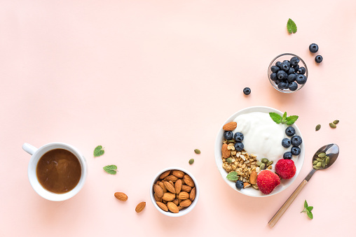 Greek yogurt with homemade granola and berries for healthy breakfast on pink pastel background, top view, copy space.
