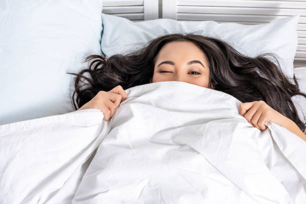istock Young beautiful asian woman winking while looking out of blanket 1145250967