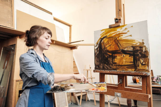 istock Young beautiful woman painter among easels and canvases in a bright studio. 1145251369