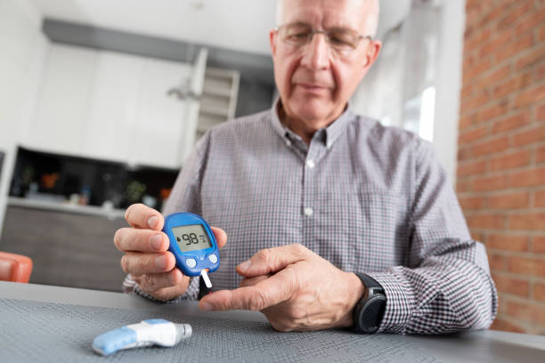 homme aîné vérifiant le niveau de sucre de sang à la maison - blood sugar test examining instrument of measurement diabetes photos et images de collection