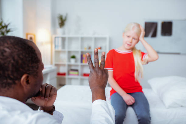 Dark-skinned doctor showing girl with concussion three fingers Three fingers. Dark-skinned doctor wearing uniform showing girl with concussion three fingers concussion stock pictures, royalty-free photos & images