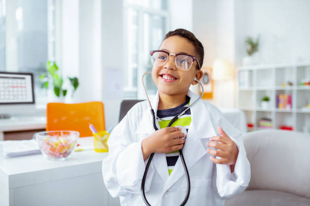 istock Cheerful boy using stethophone and wearing white jacket of doctor 1145261664