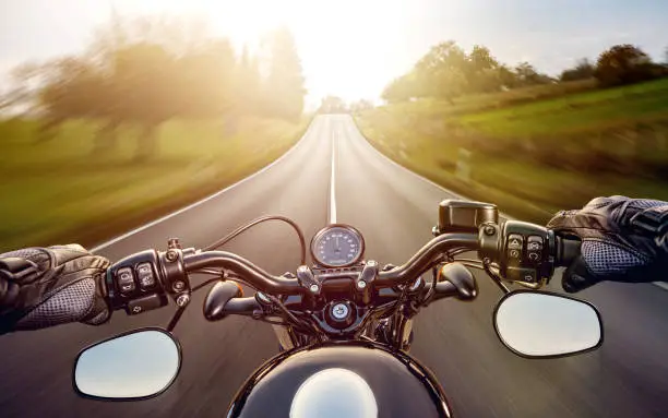 Photo of POV shot of young man riding on a motorcycle. Hands of motorcyclist on a street