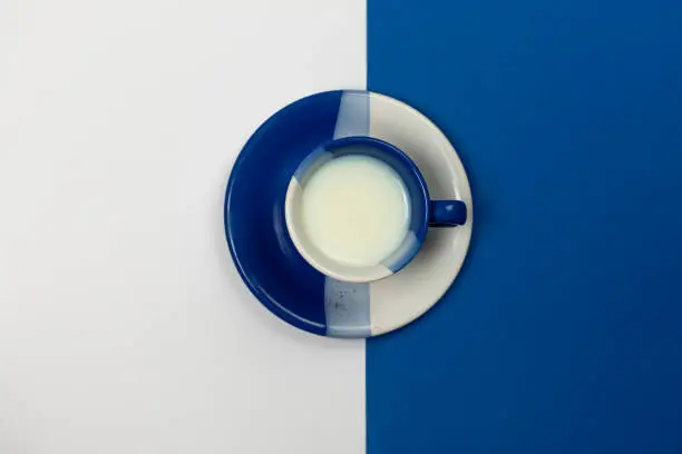 Blue and White coffee mug filled with fresh milk resting on a blue and white background