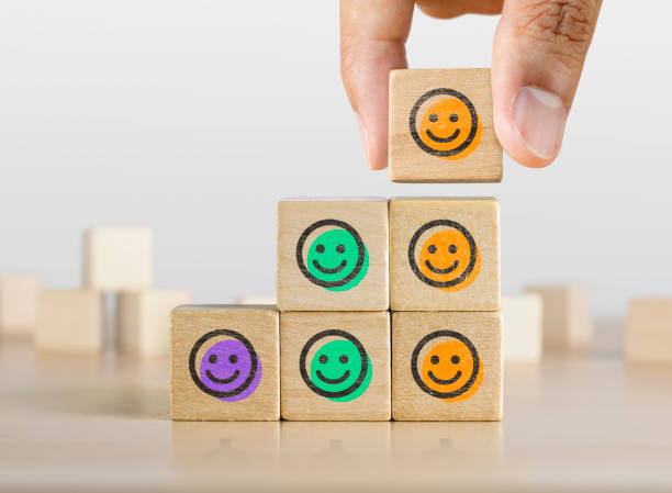 Positive attitude, customer satisfaction, emotional management or happiness concept. Wooden blocks with happy face emotion graphic arranged in stair shape and a man is holding the top one. stock photo
