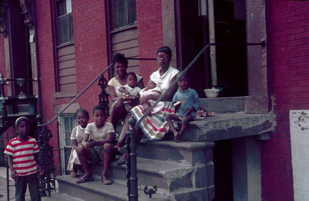 zwei mütter mit ihren kindern sitzen auf der treppe vor ihrem mietshaus, new york city - archivmaterial stock-fotos und bilder