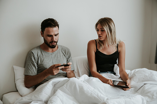 Young Couple Sharing Information while Using Smartphone in Bed