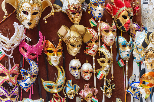 Young woman taking a photo of Venetian masks on display in illuminated street retail, visiting Venice, Italy in time of Carnival