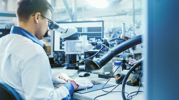 elektronikfactory arbeiter in white work coat inspect a printed circuit board through a digital microscope. high tech factory facility. - halbleiter fotos stock-fotos und bilder