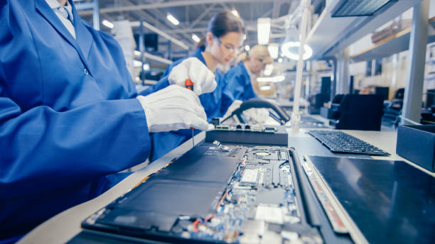 närbild av en kvinnlig elektronik fabriks arbetare i blått arbete coat montering laptop ' s moder kort med en skruvmejsel. high tech fabriks anläggning med flera anställda. - löpande band bildbanksfoton och bilder