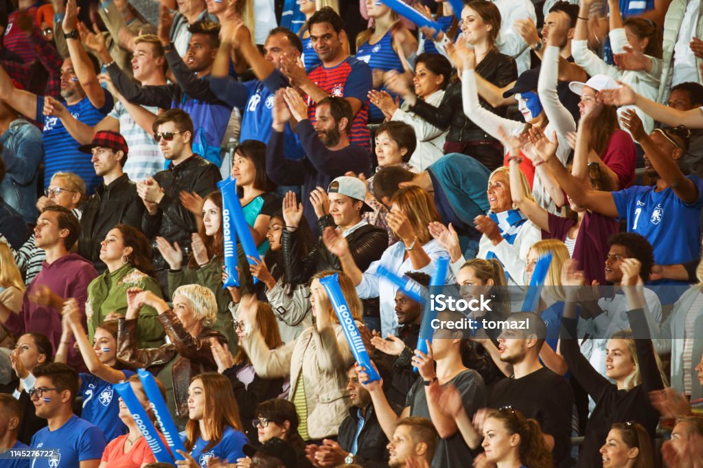 Spectators clapping on a stadium Large number of spectators on a match clapping, smiling and cheering for the blue team. Soccer Stock Photo