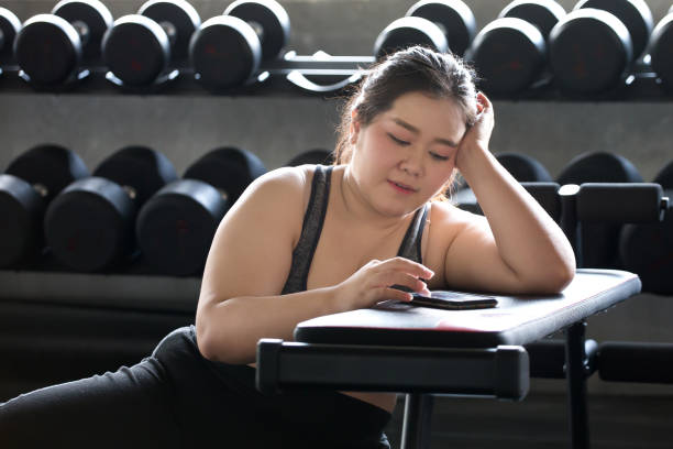 young asian fitness woman using smartphone and relaxing in gym . sport  Overweight girl taking a break after exercises workout . obese female resting . chubby give up. lifestyle stock photo